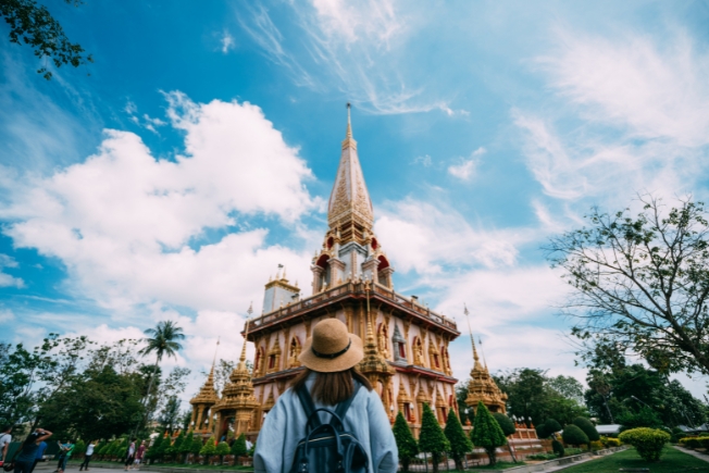 Arooha guest young woman traveler with backpack traveling into beautiful pagoda in temple at Phuket