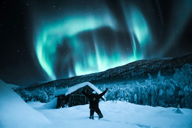 Arooha traveler standing in snowy field under Northern Light in Norway