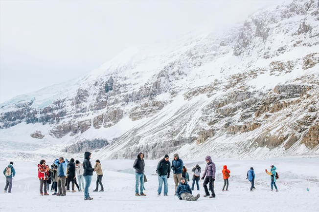 A group of people dressed in winter clothing enjoying snow activities in a scenic, snow-covered mountainous area in Norway.